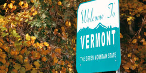 Welcome sign of the state of Vermont set against backdrop of fall leaves