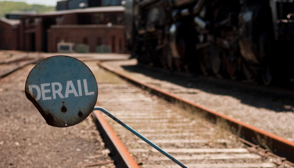 Circular sign above railroad tracks with white letters stating derail