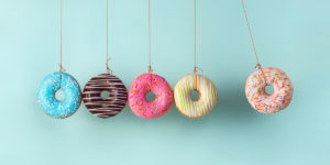 Baby blue background with five different colored iced donuts hanging from twine. Four are together on the left, with one apart from the four as if separated. Under the four donuts that are together is the word Nope in black text.g
